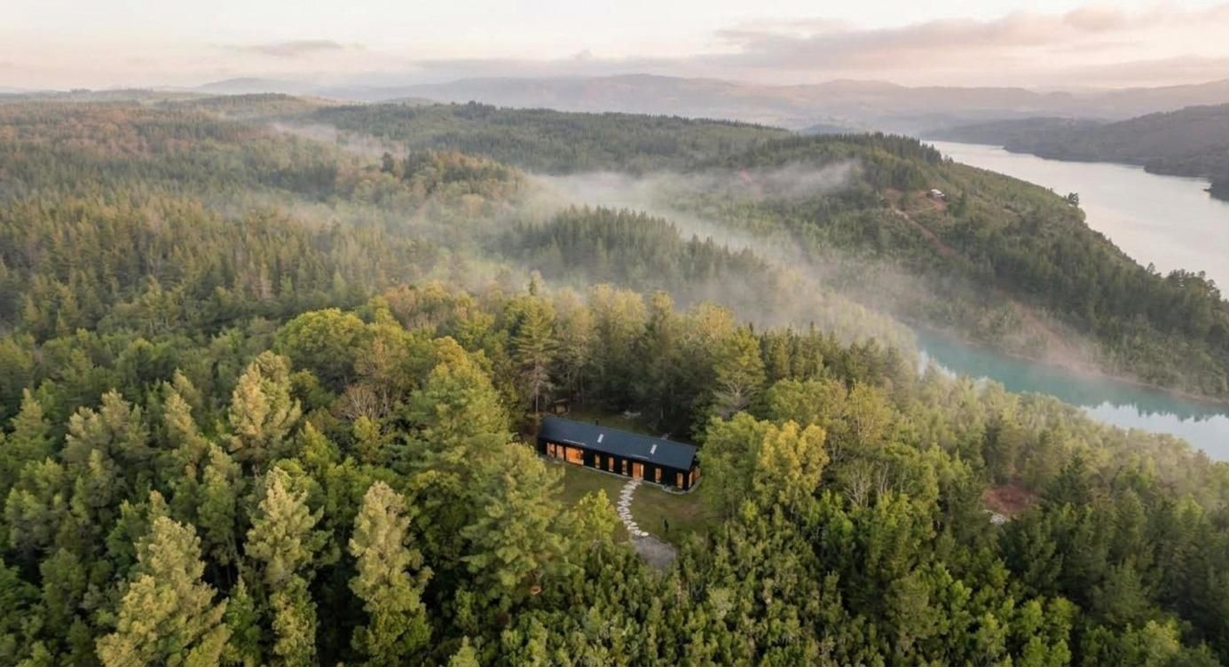 Vista aérea de una cabaña entre el bosque con el Embalse Digua al fondo